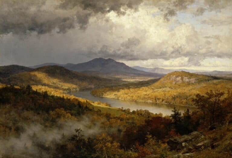 Ein Fluss schlängelt sich durch eine sonnenbeschienene Herbstlandschaft mit bunten Bäumen, sanften Hügeln und fernen Bergen unter einem dramatisch bewölkten Himmel. Aus dem bewaldeten Tal im Vordergrund steigt Nebel auf.