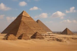 Das Bild zeigt die Pyramiden von Gizeh in Ägypten, mit mehreren großen und kleinen Pyramiden, die in einer Sandwüste unter einem blauen Himmel mit vereinzelten Wolken stehen.