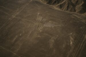 Luftaufnahme der Nazca-Linien in Peru, mit einer großen Geoglyphe eines stilisierten Kolibris, der in die trockene, braune Wüstenlandschaft geätzt wurde, mit Bergen im Hintergrund.
